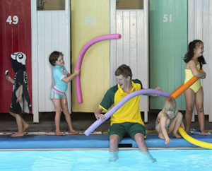 Children playing at a pool with pool noodles